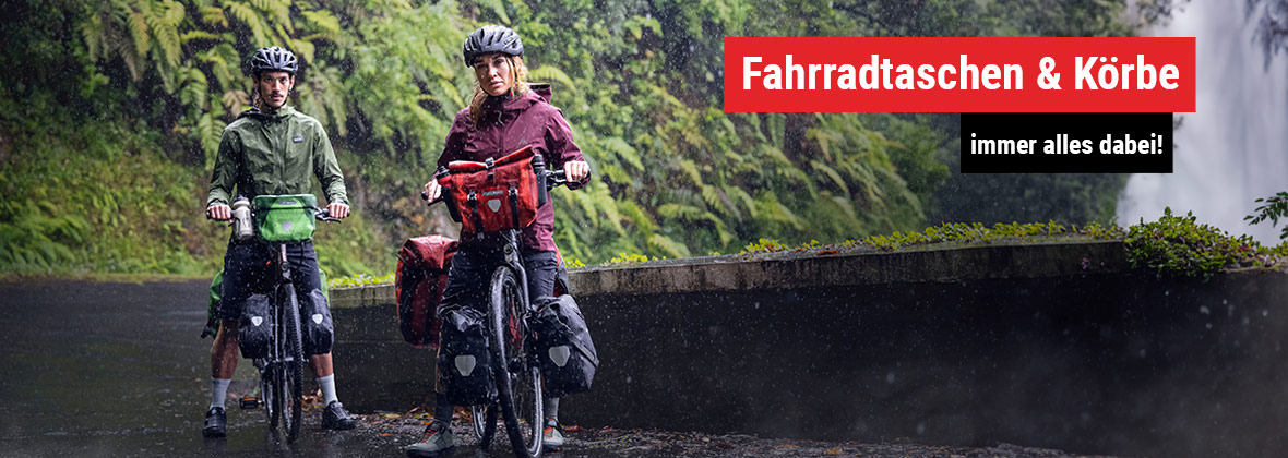 Mann und Frau stehen mit ihren Fahrrädern im Regen vor grüner Vegetation.