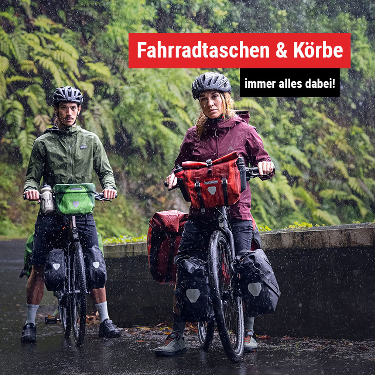 Mann und Frau stehen mit ihren Fahrrädern im Regen vor grüner Vegetation.