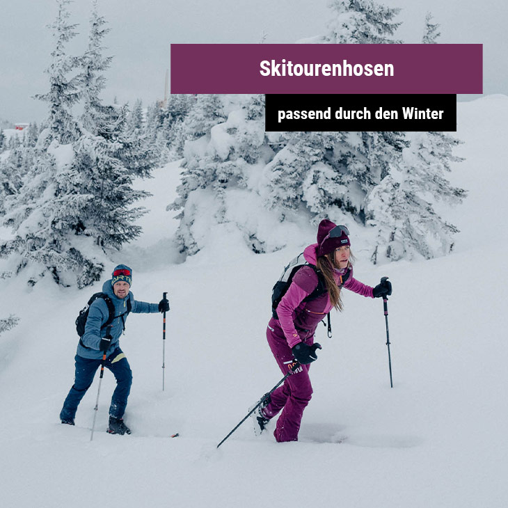 Eine Frau und ein Mann die mit Tourenski auf einen Berg steigen 
