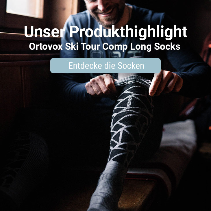 Mann der sich in einem Haus Socken von der Marke Ortovox anzieht und dabei fröhlich aussieht 