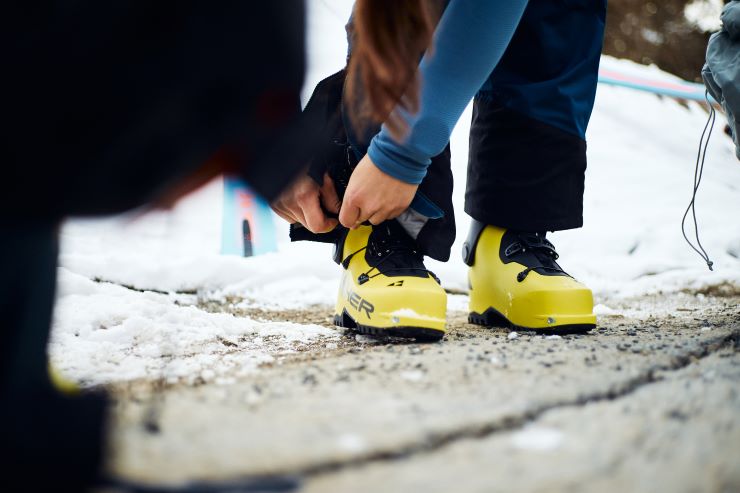 Eine Person schnürt Skistiefel im Schnee für eine Tourenvorbereitung.