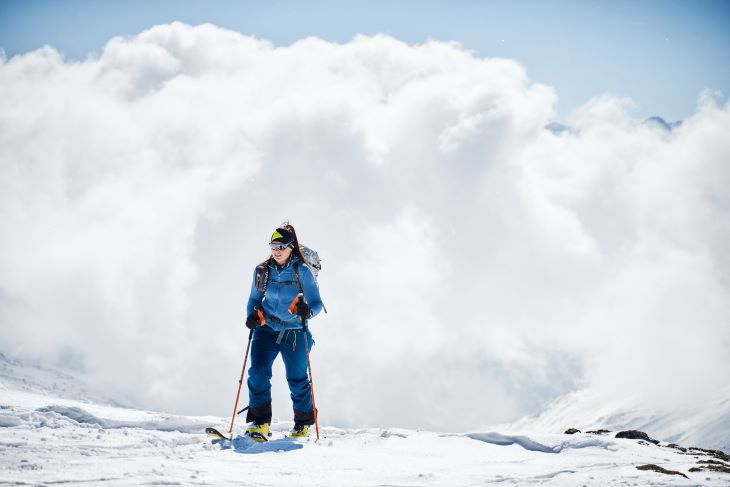 Skitourengeherin steht auf einem verschneiten Berg vor einer dramatischen Wolkenkulisse.